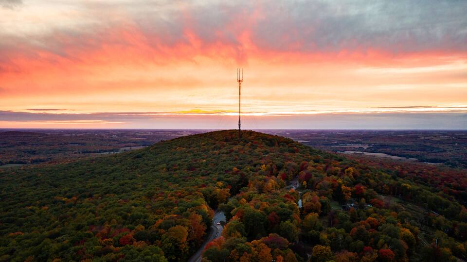 A hilltop with a communication tower, surrounded by autumn-colored trees and a winding road.