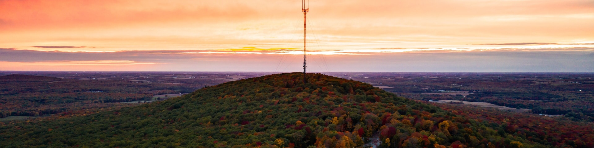 Una colina con una torre de comunicaciones, rodeada de árboles de colores otoñales y un camino sinuoso.