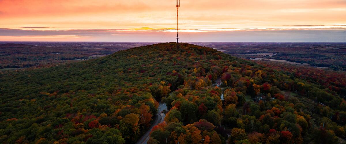 A hilltop with a communication tower, surrounded by autumn-colored trees and a winding road.