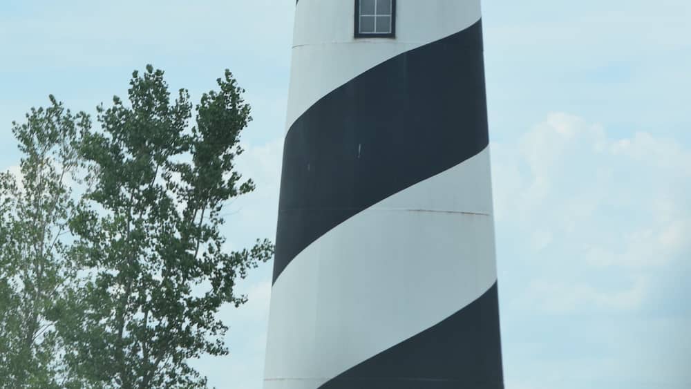 A lighthouse with black and white stripes, a red roof, and the words "STORM LAKE" on a stone wall in front.