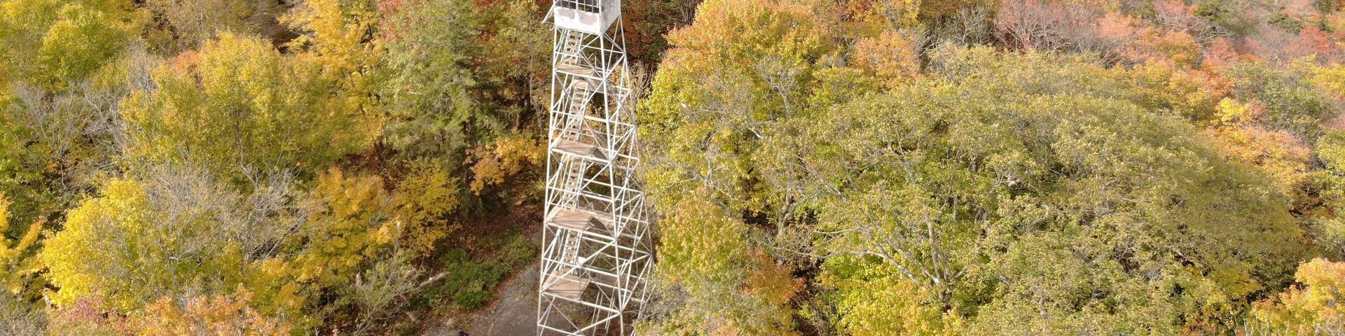 Aerial of Kane Mountain Fire Tower with autumn forest scape water near Fulton County, New York