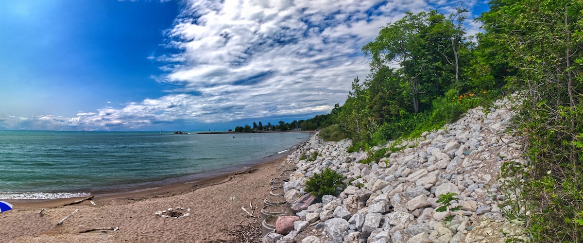 A rocky beach with a clear view of the sea, a partly cloudy sky, and dense greenery on the right.