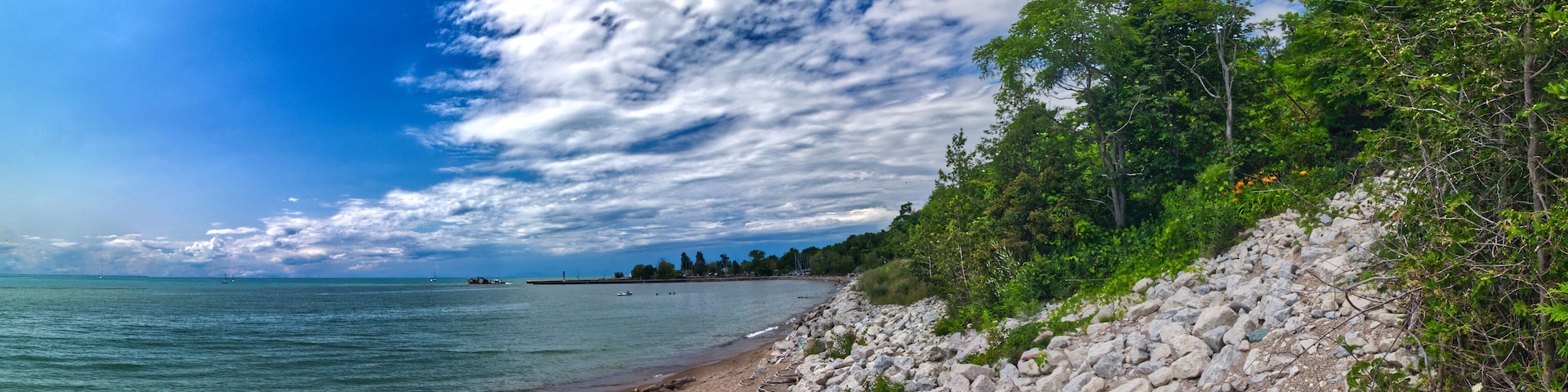 A rocky beach with a clear view of the sea, a partly cloudy sky, and dense greenery on the right.