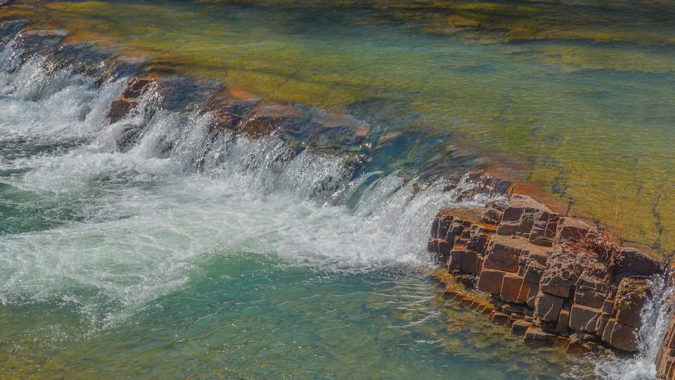 A waterfall cascading over rocks into clear, turquoise water.