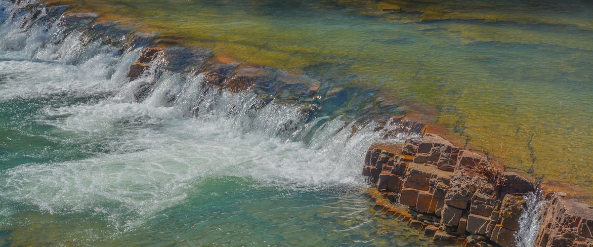A waterfall cascading over rocks into clear, turquoise water.