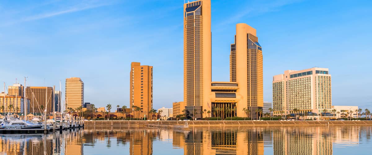A city skyline with tall buildings reflected in calm water.