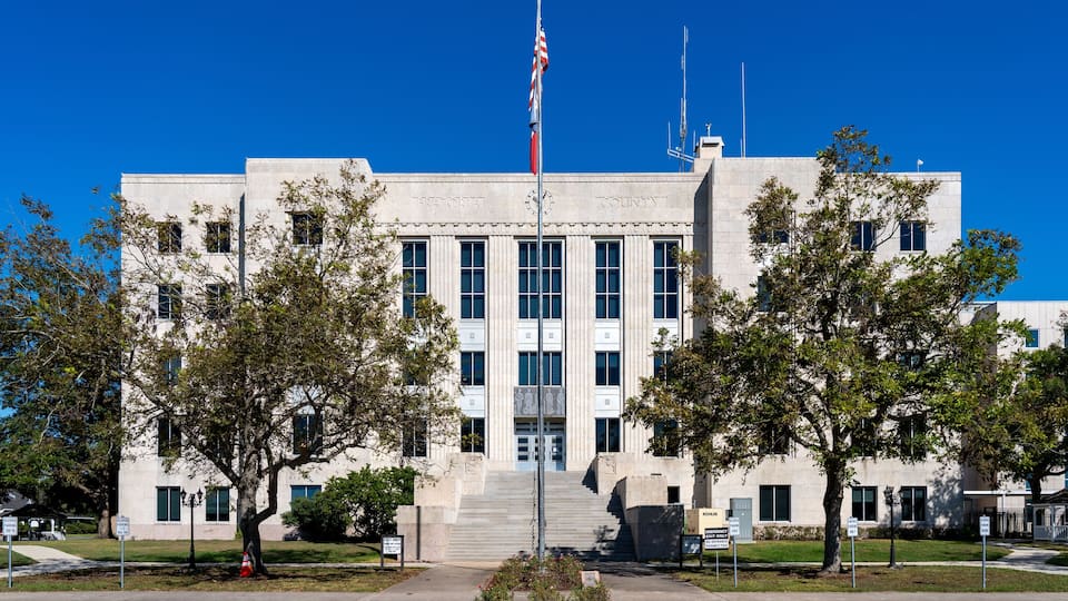 A government building with a flagpole, steps leading to the entrance, and trees in front.