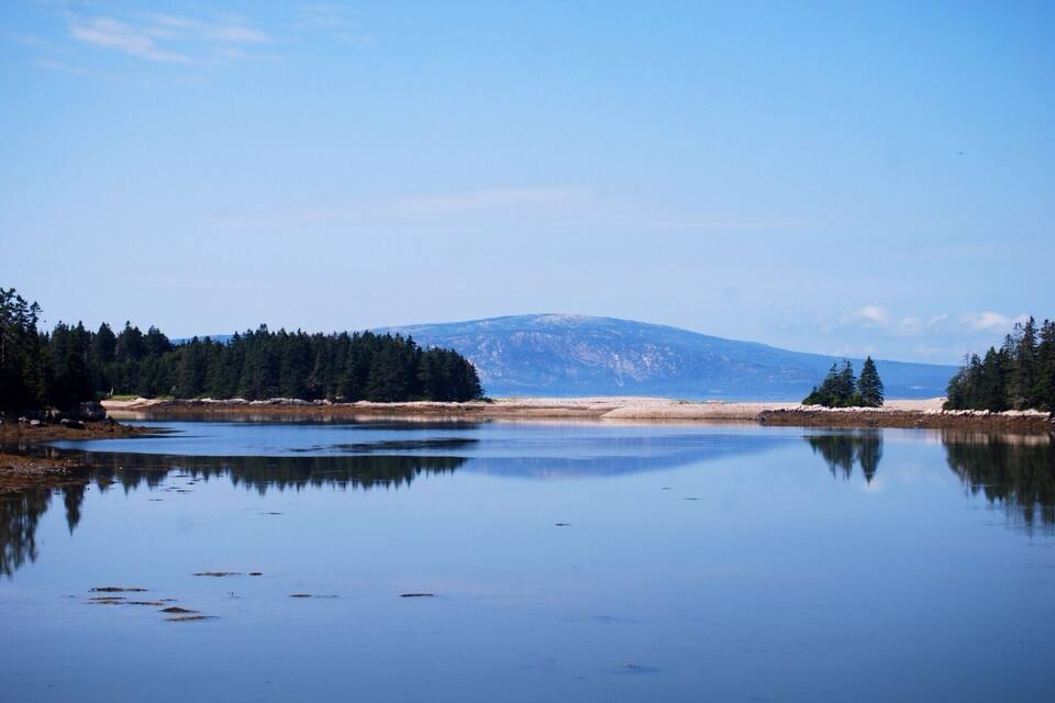 A calm lake with a forested shoreline and a mountain in the background.