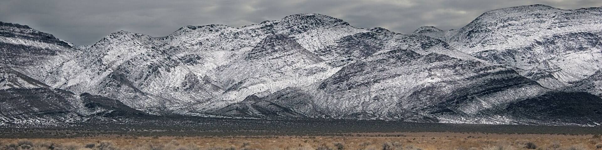 A snow-covered mountain range with a dry, grassy foreground.