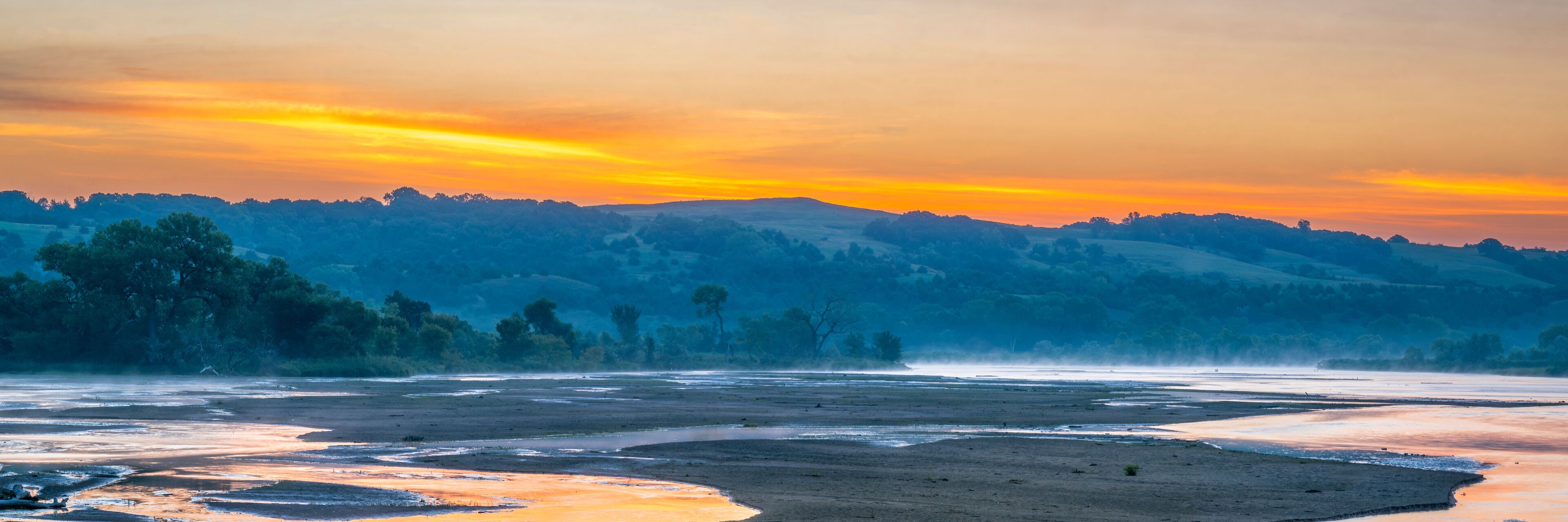 A river at sunset with hills in the background.