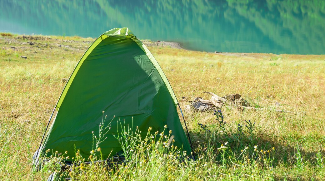 a tent stands on the shore of a beautiful pond surrounded by mountains