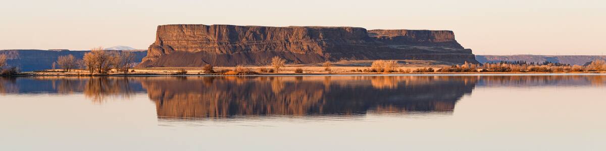 A calm lake reflecting a flat-topped plateau with sparse vegetation.