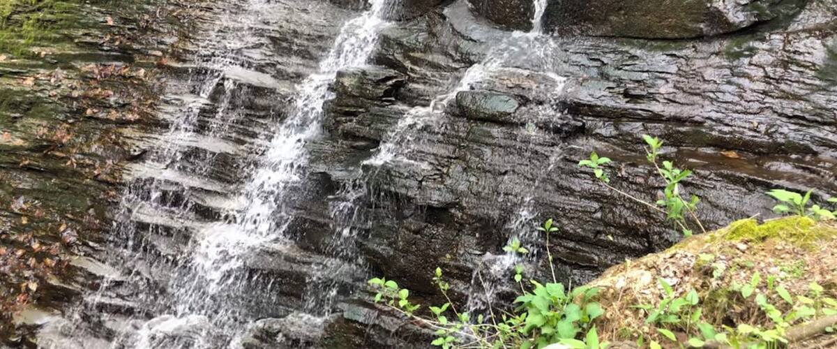 A cascading waterfall over rocky terrain with moss-covered rocks and some greenery at the base.