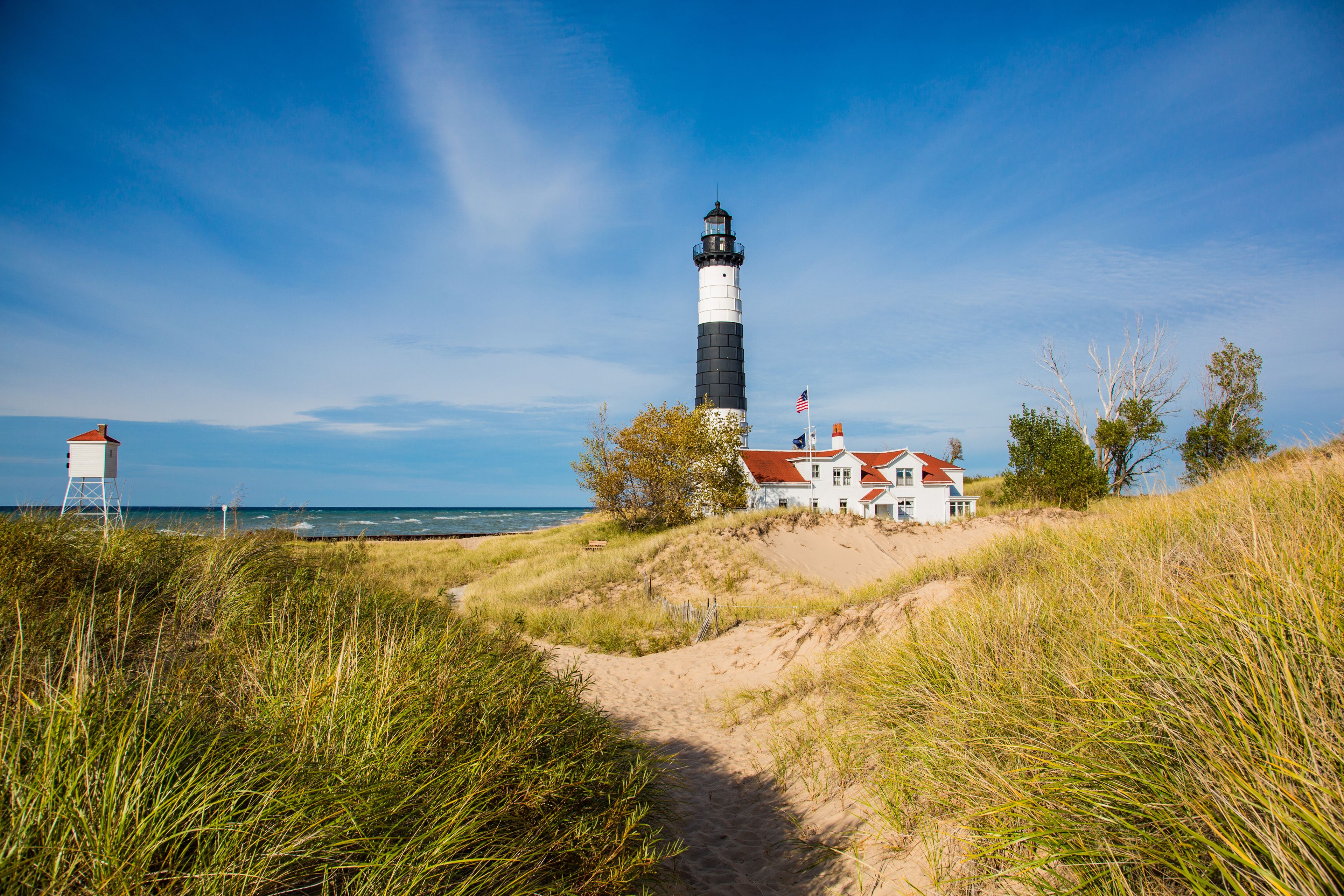 A lighthouse, a white building with a red roof, and a sandy path leading to the building.