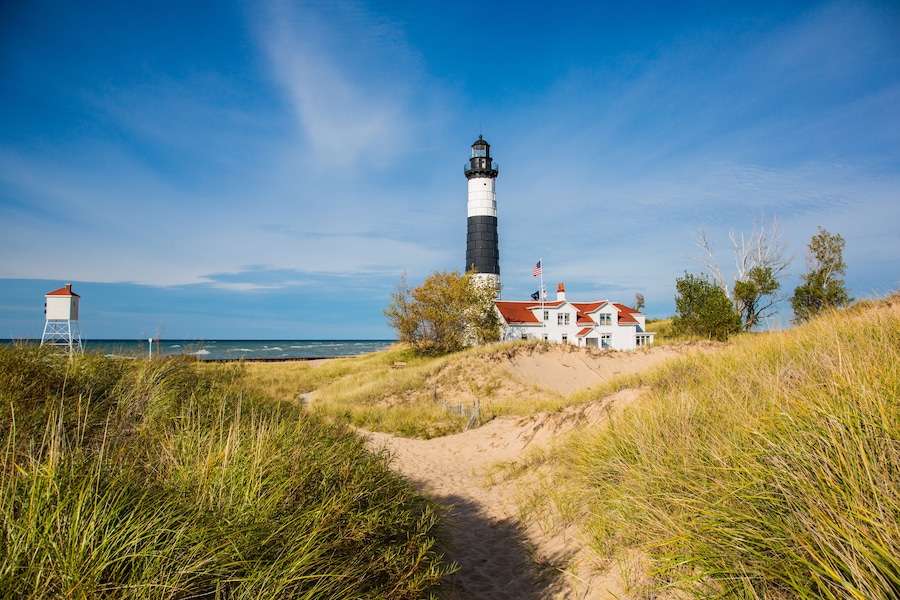 A lighthouse, a white building with a red roof, and a sandy path leading to the building.