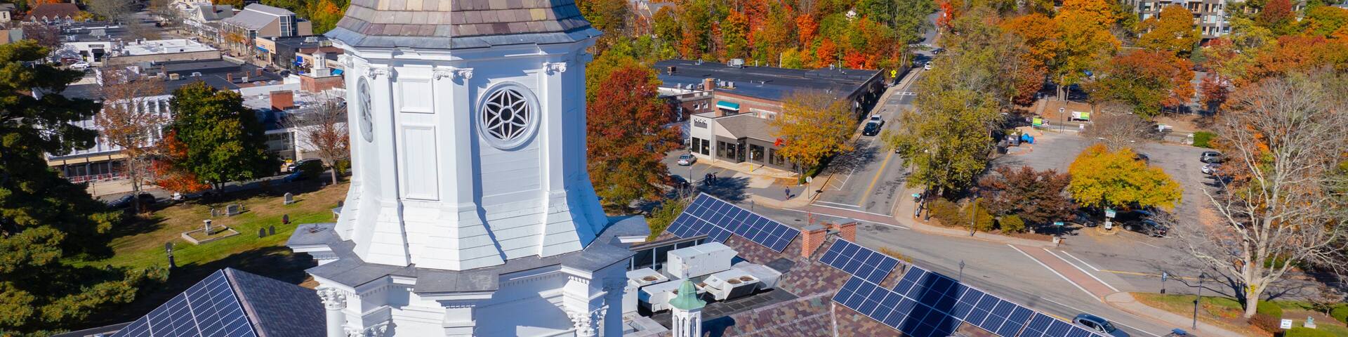 A church with a steeple, solar panels, and autumn foliage in the background.