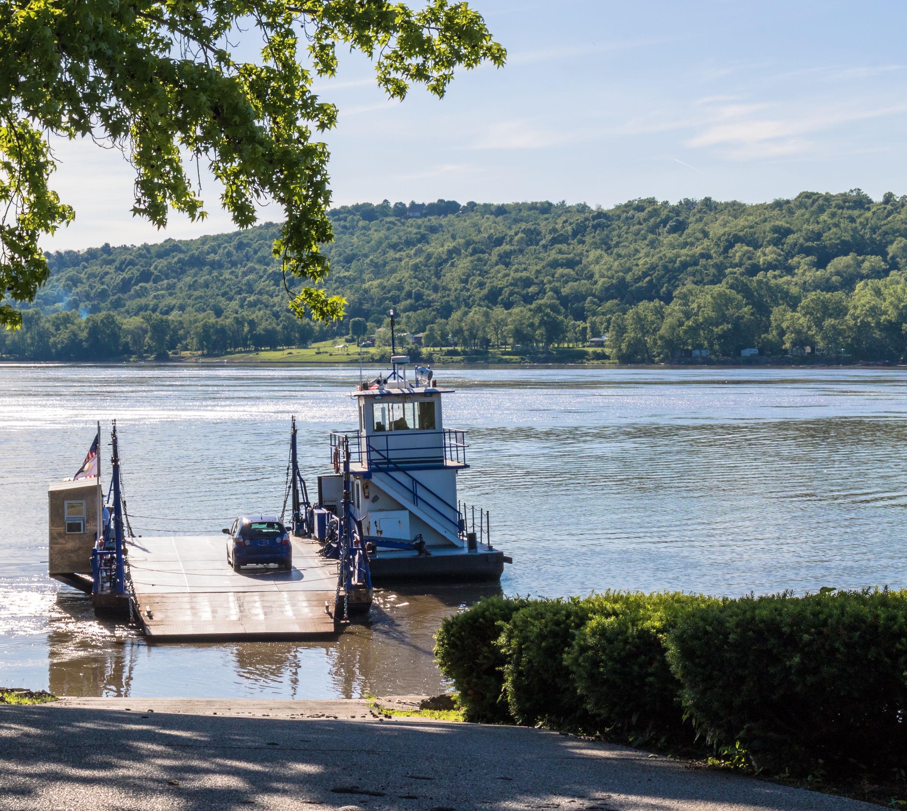 A ferry dock with a boat, a river, and a forested hillside in the background.