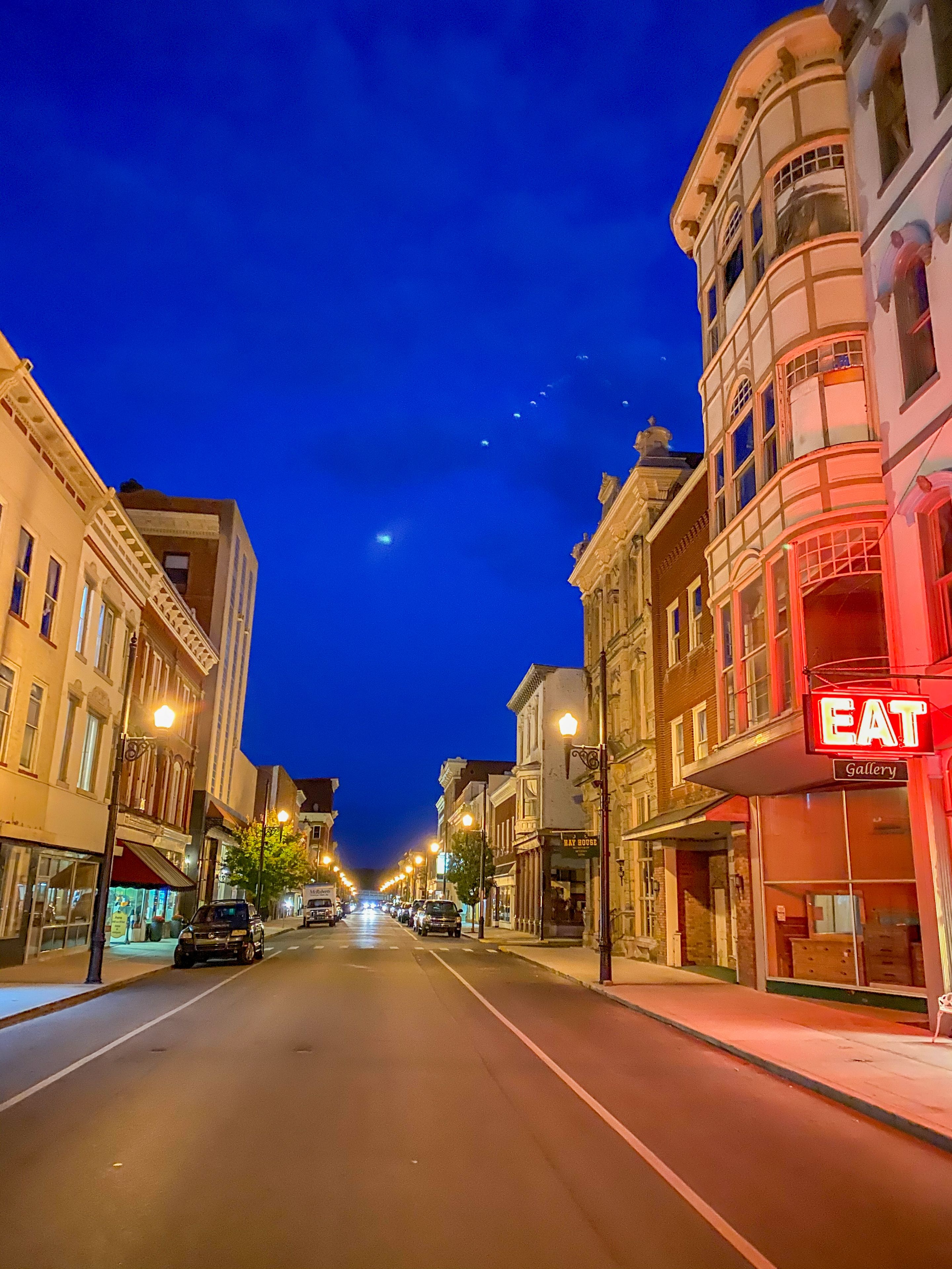 A street lined with historic buildings, a prominent red 'EAT' sign, and a clear night sky.