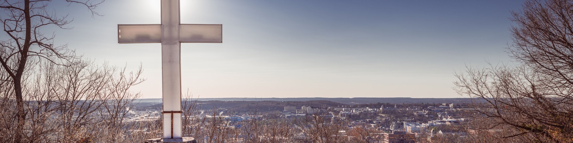 A cross on a stone pedestal with a cityscape in the background.