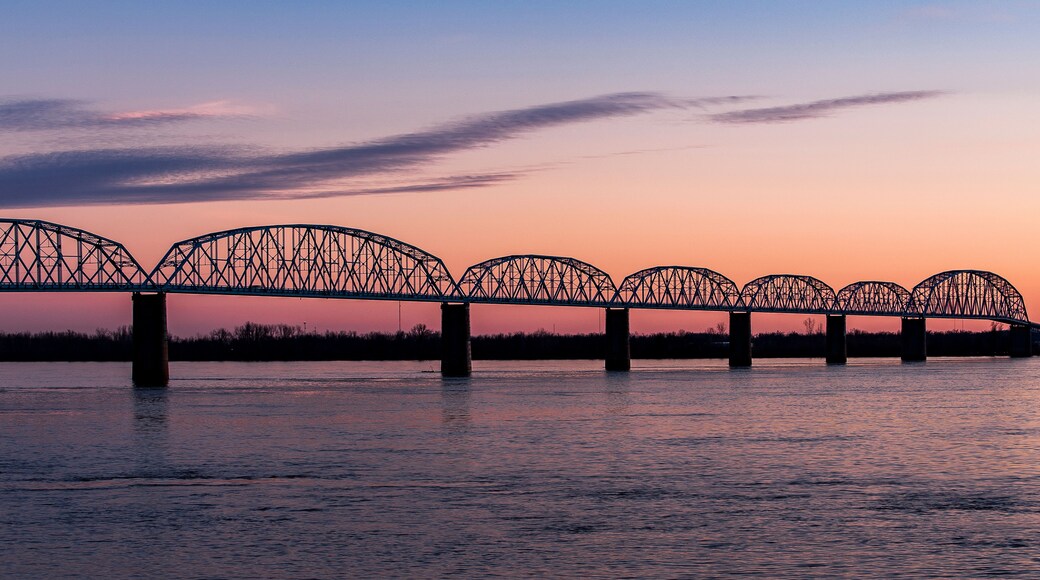 A steel bridge with multiple arches over a body of water during sunset.