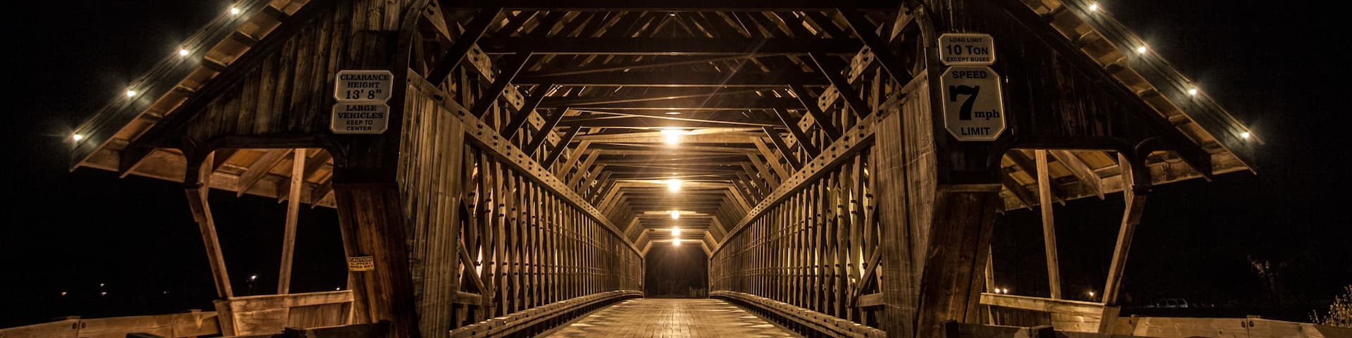 A wooden covered bridge with lights, a sign indicating a 10-ton vehicle limit, and a speed limit of 7 mph.