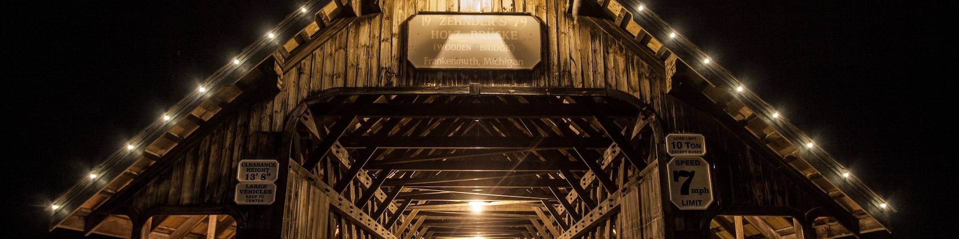 A wooden covered bridge with lights, a sign indicating a 10-ton vehicle limit, and a speed limit of 7 mph.