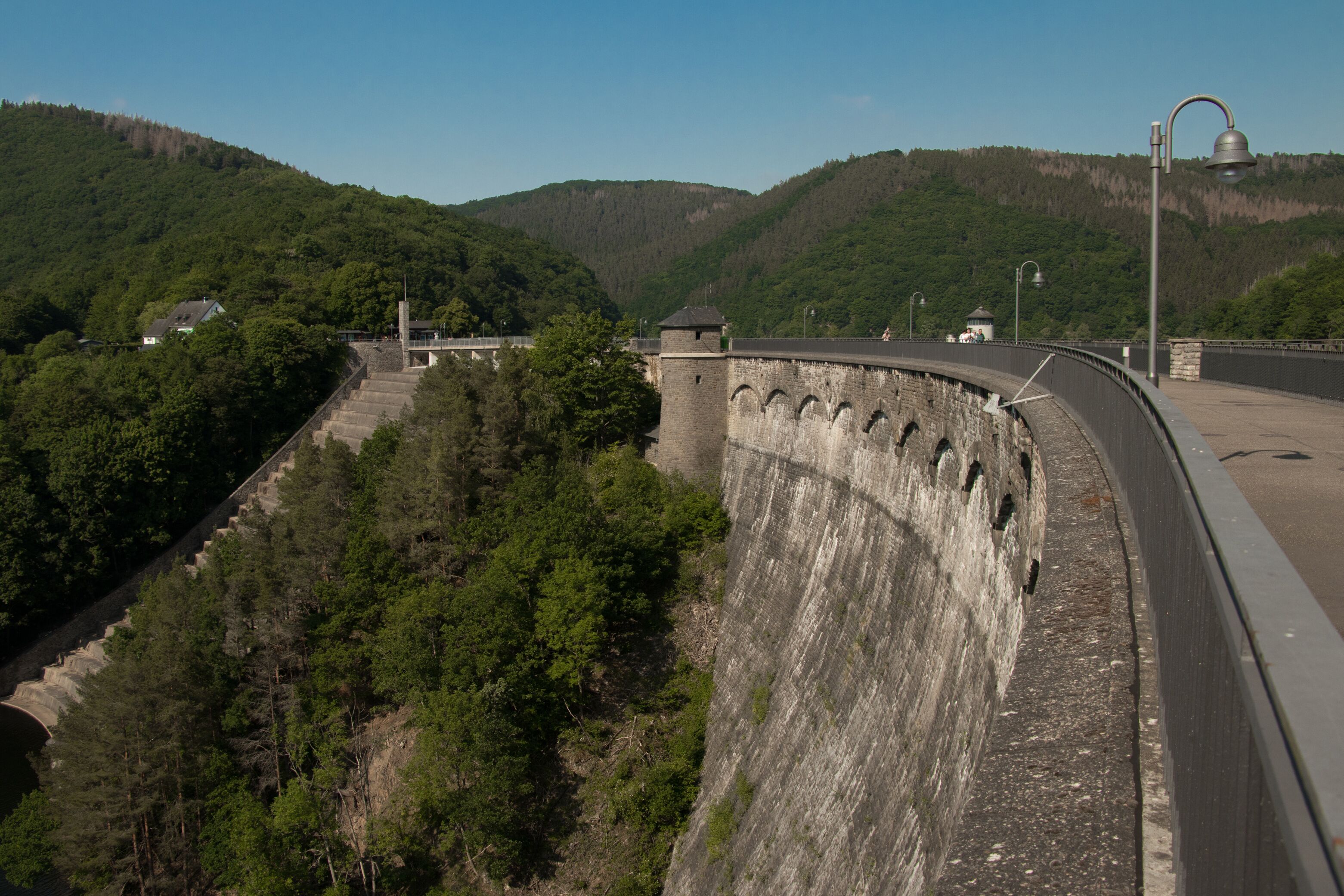 Un barrage doté d’un mur incurvé, un pont et une colline boisée.