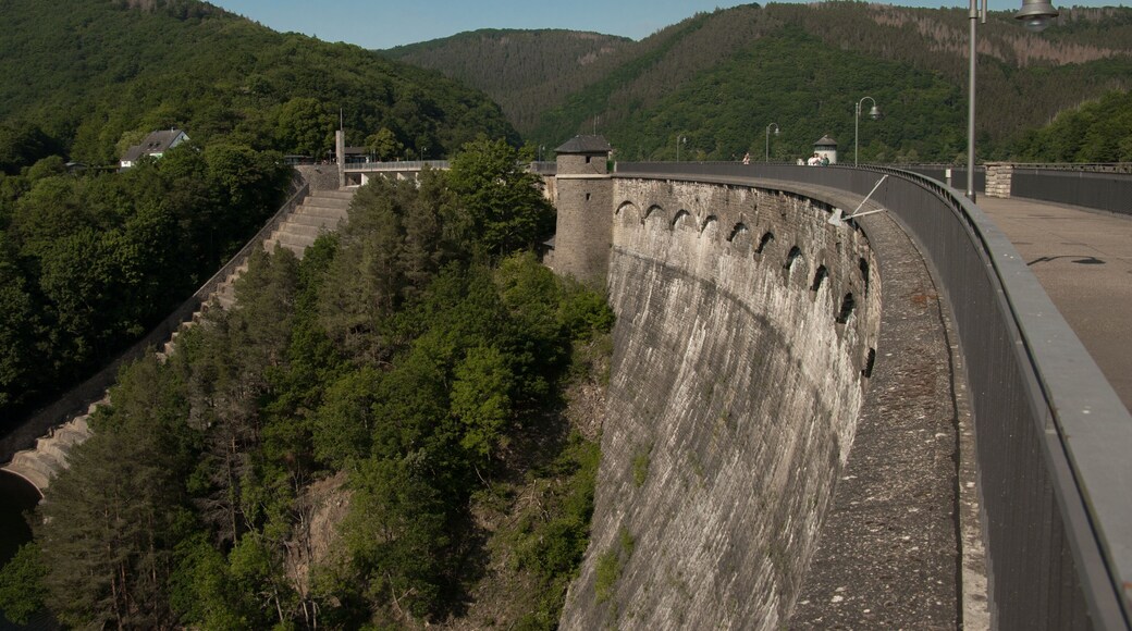 Un barrage dotĂ© dâun mur incurvĂ©, un pont et une colline boisĂ©e.