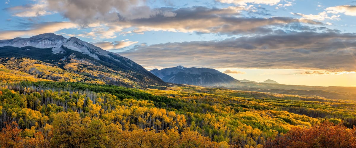 A mountainous landscape with autumn foliage and a sunset.
