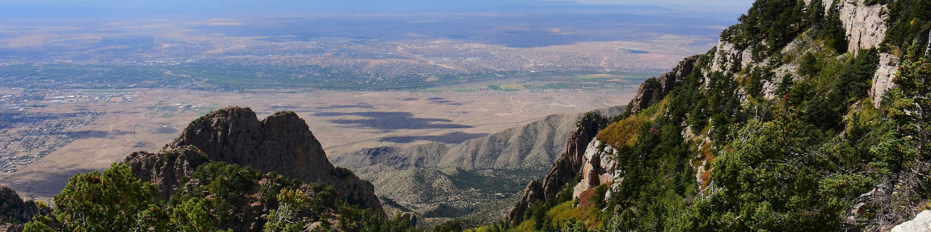 Paisagem montanhosa com florestas densas, afloramentos rochosos e uma vista distante de um vale.