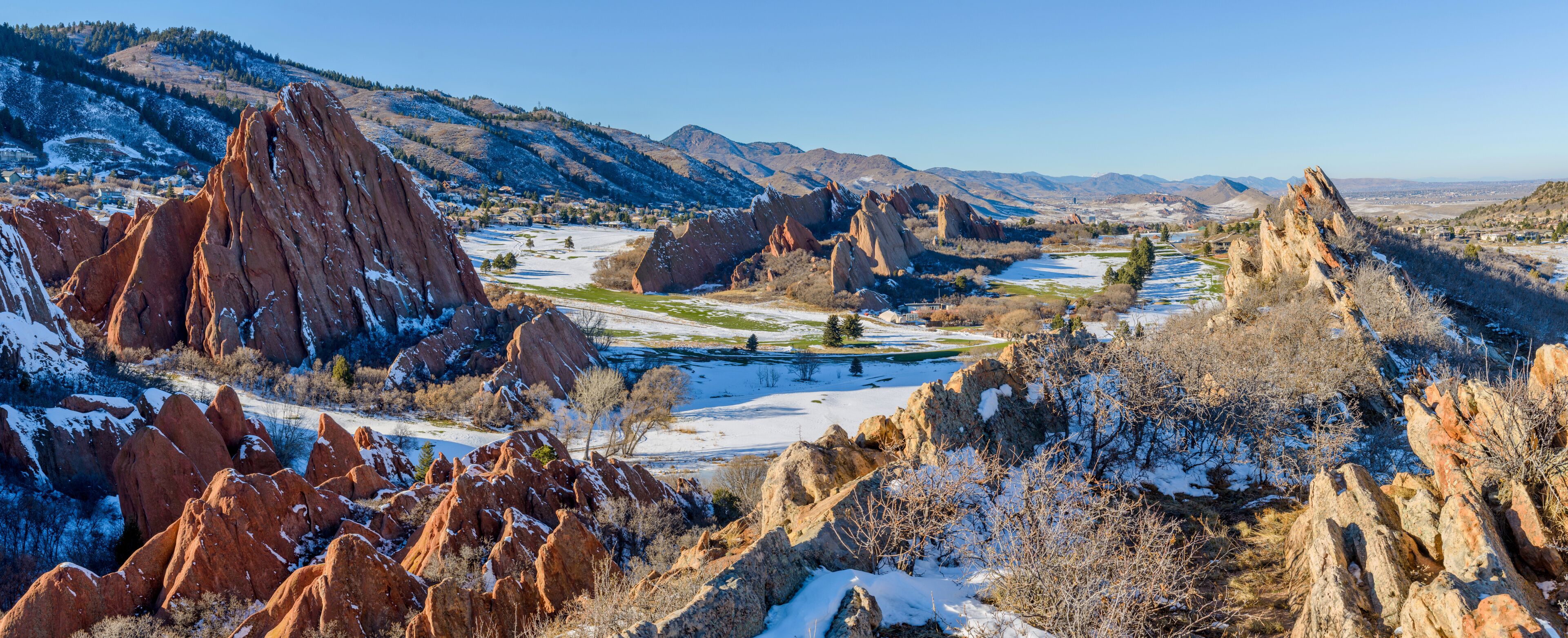 A snow-covered landscape with prominent red rock formations and a distant view of a valley.
