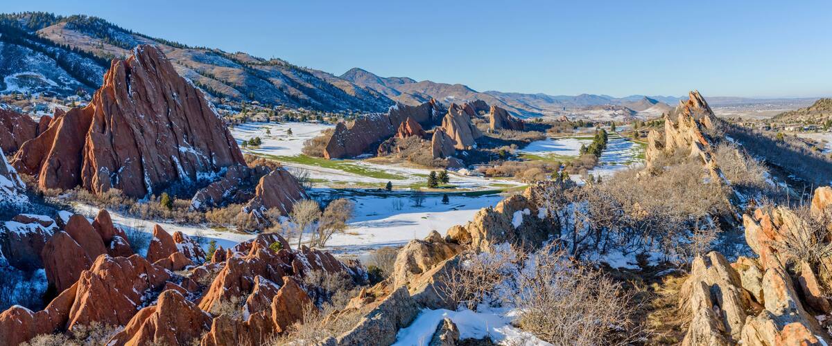 A snow-covered landscape with prominent red rock formations and a distant view of a valley.