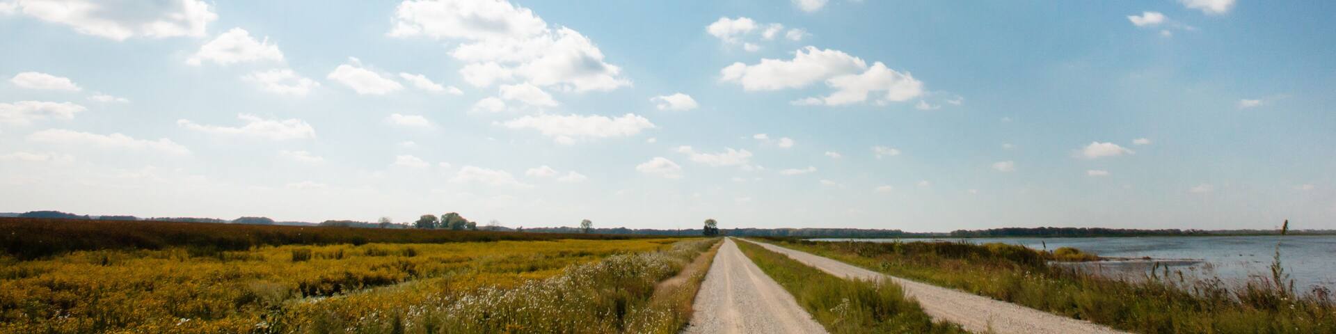 A rural road leading to a body of water under a clear sky.