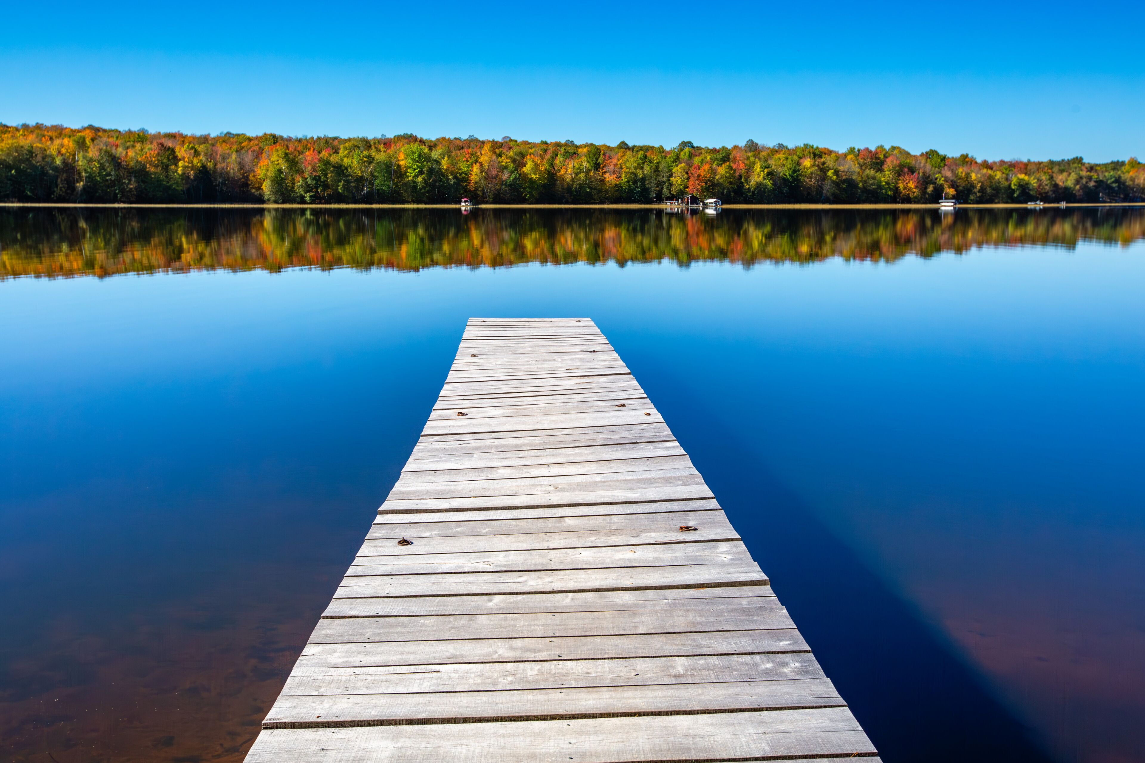 A wooden pier extending into calm water with a forested shoreline reflecting in the water.