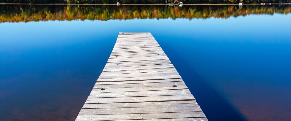 A wooden pier extending into calm water with a forested shoreline reflecting in the water.