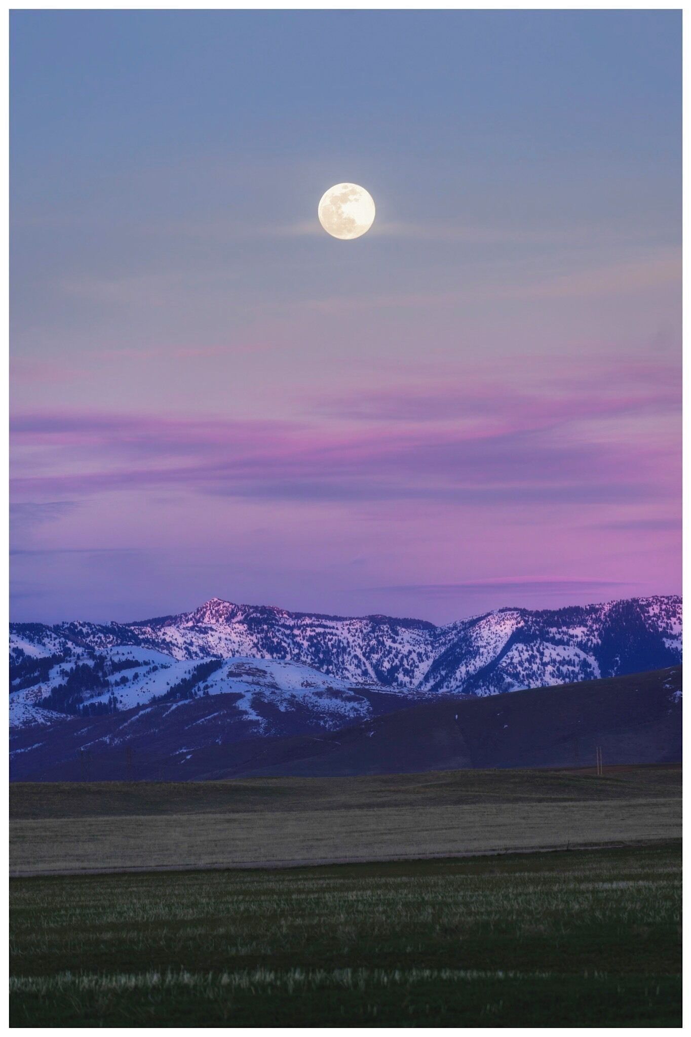 A full moon over snow-covered mountains with a purple sky.