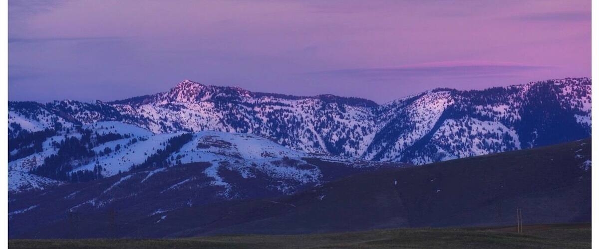 A full moon over snow-covered mountains with a purple sky.