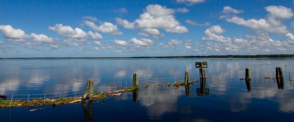 Ein ruhiger See unter blauem Himmel mit vereinzelten Wolken.