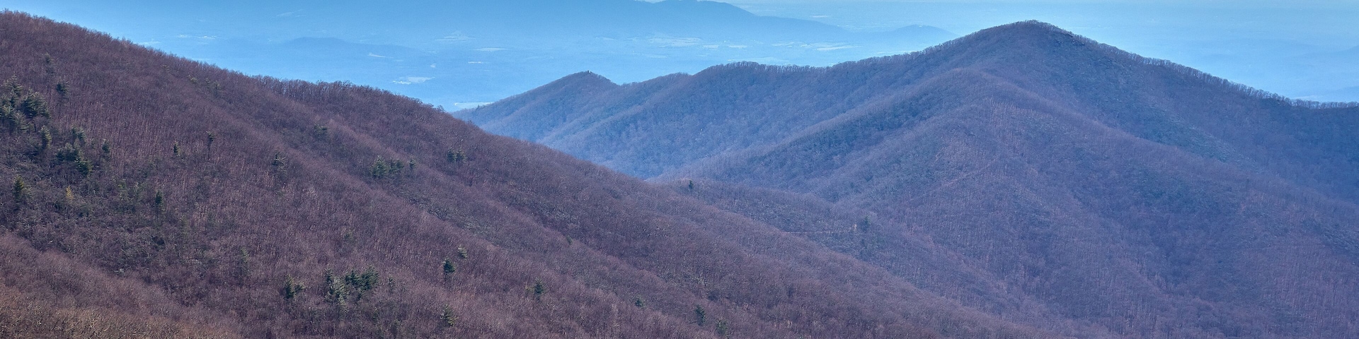 A mountainous landscape with dense forests and distant mountain ranges.