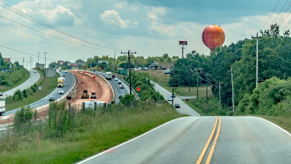 A highway with a roundabout, a construction site, and a large hot air balloon in the distance.