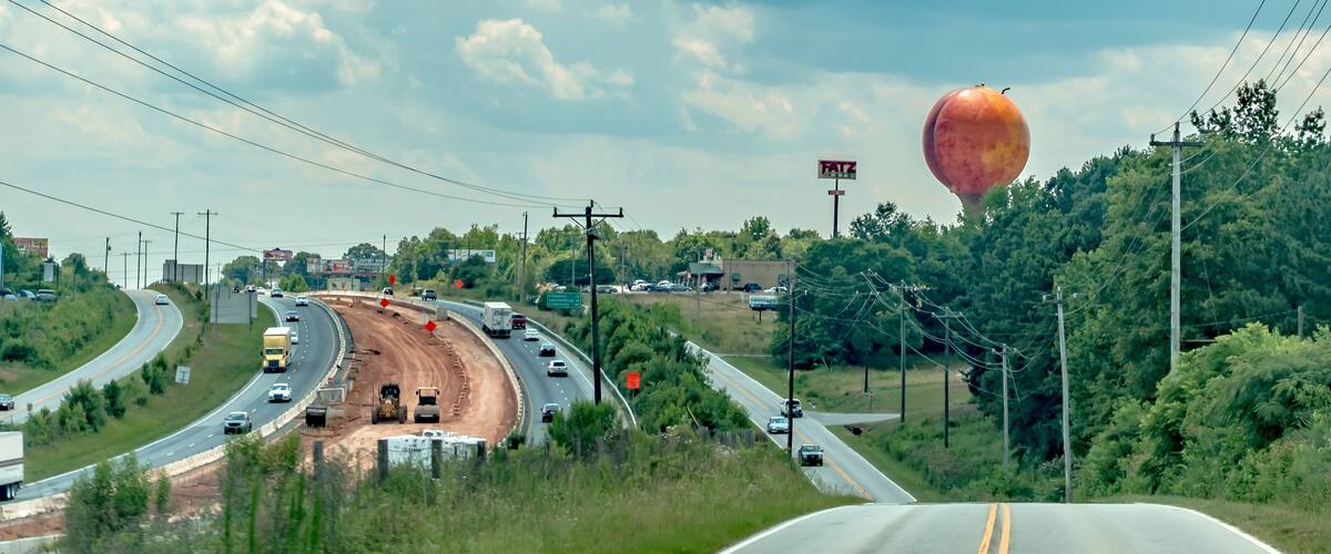A highway with a roundabout, a construction site, and a large hot air balloon in the distance.