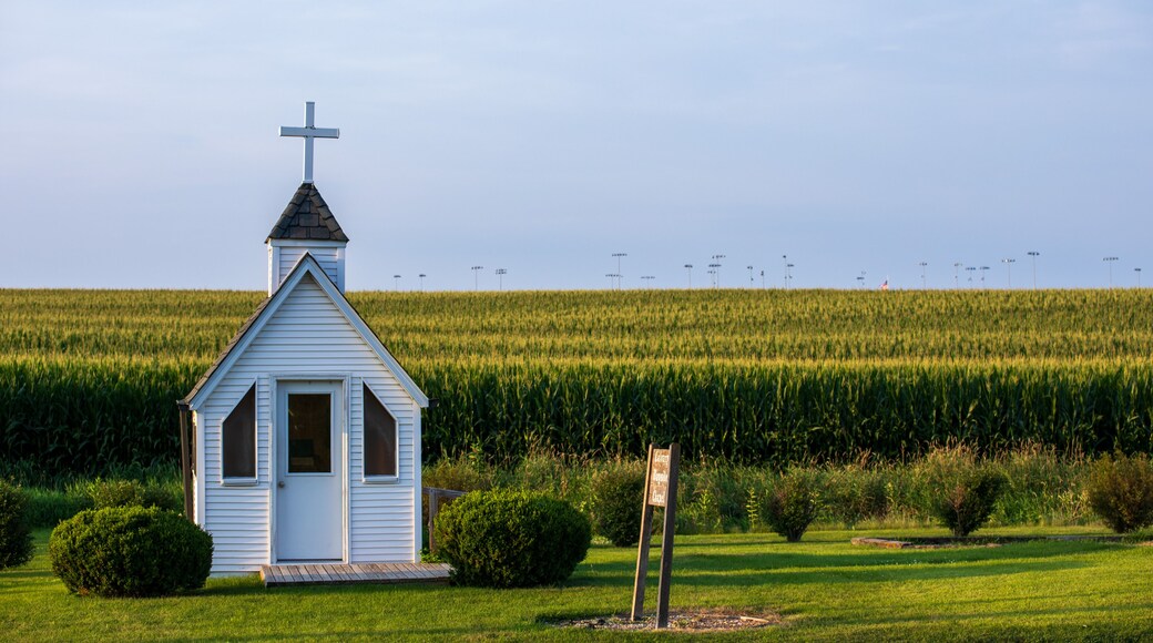 Een witte kerk met een kruis, omringd door een akker en een heldere lucht.
