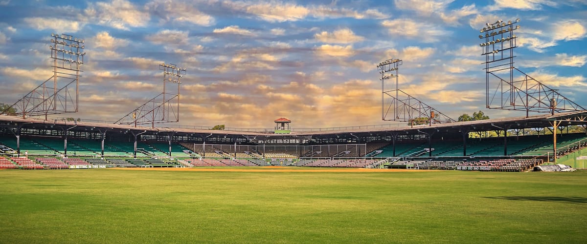 A large, empty sports stadium with green seating and floodlights.
