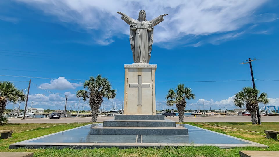 A statue with outstretched arms, palm trees, and a clear blue sky.