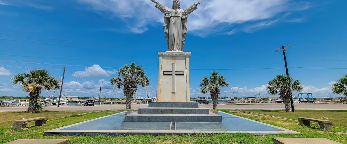 A statue with outstretched arms, palm trees, and a clear blue sky.