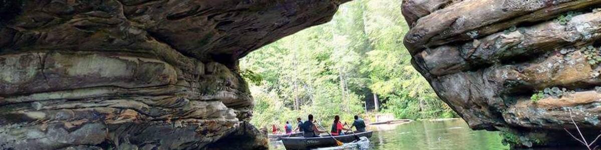 A rock arch over a river with people in a boat.