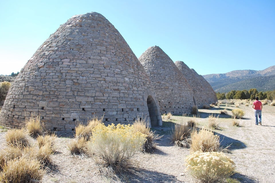 Stone structures with a conical shape, surrounded by dry grass and shrubs.