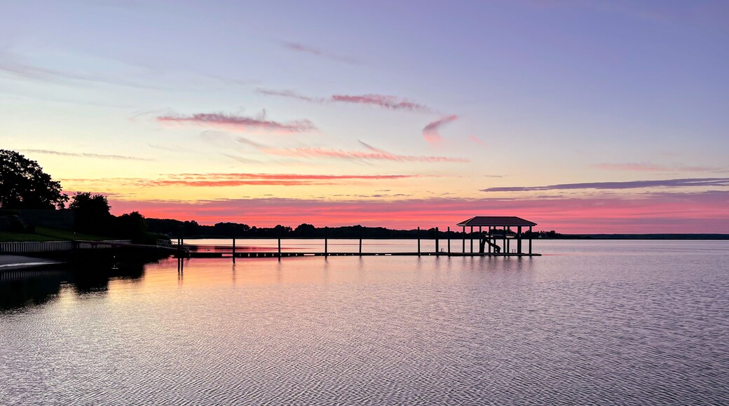 A sunset over a calm lake with a pier and a gazebo.