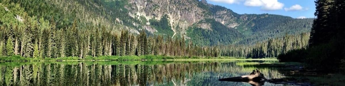 Ein Bergsee mit klaren Spiegelungen, umgeben von dichten Wäldern und felsigen Bergen.