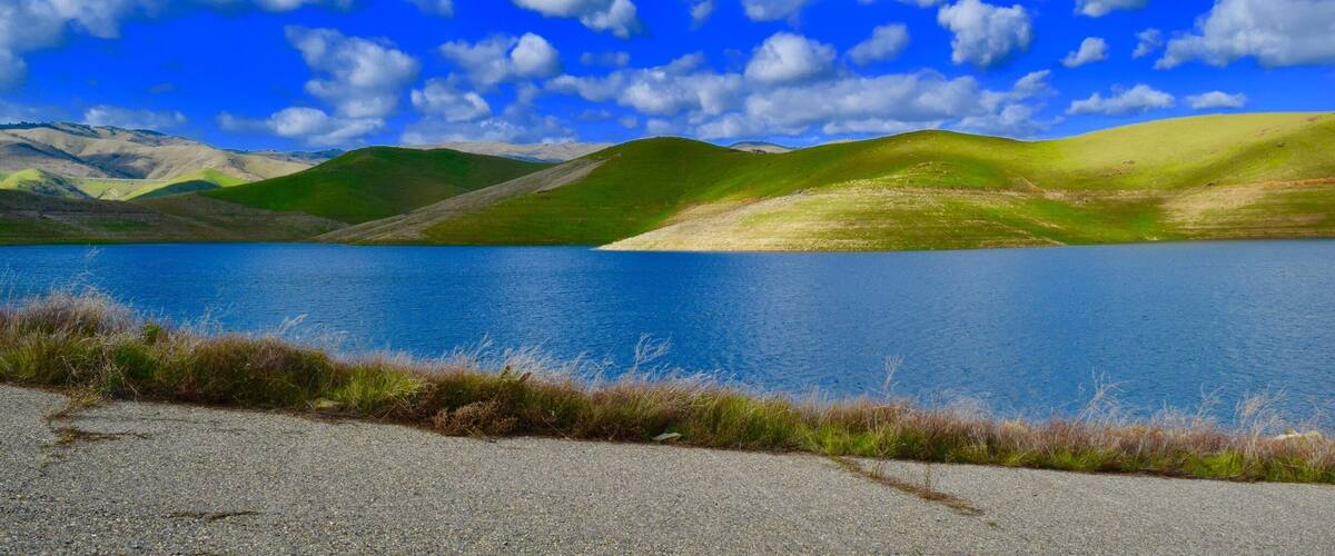 A lake surrounded by green hills under a blue sky with clouds.